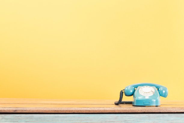 复古的绿松石旋转电话在木桌前黄墙背景。老式滤镜照片图片下载