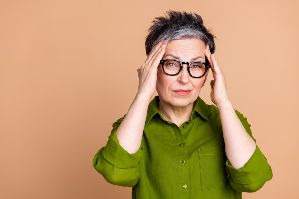 照片肖像漂亮的高级女性触摸太阳穴头痛穿时髦的绿色服装孤立的米色背景图片下载