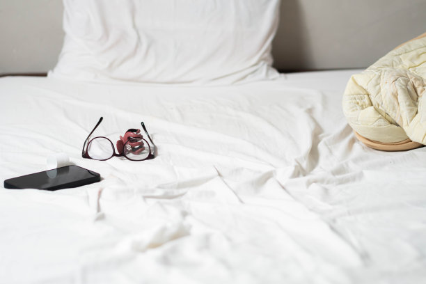 眼镜和智能手机躺在白色的床上图片下载