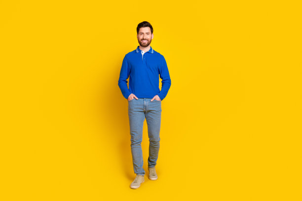 漂亮的年轻男性走路摆姿势模特的全尺寸照片，穿着时髦的蓝色服装，孤立在黄色背景上图片下载