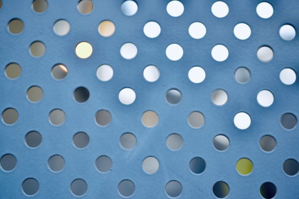 一张带有圆形孔的蓝色穿孔金属片的特写照片。图片下载