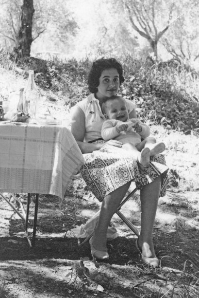 这张照片拍摄于1960年，照片中，一位面带微笑的年轻女子坐在露营椅上，抱着她的男婴看着镜头图片下载