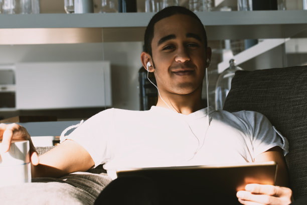 年轻人躺在沙发上玩着数码平板电脑，喝着咖啡图片下载