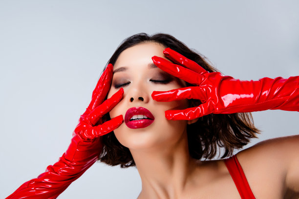 照片上迷人的年轻女子抚摸着脸，闭着眼睛，穿着红色的皮衣，孤立在浅灰色的背景上图片下载