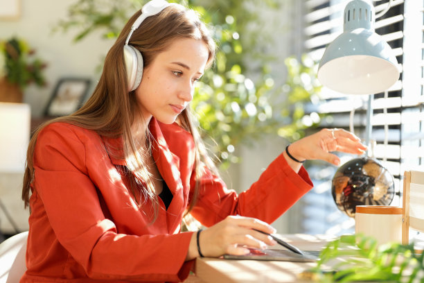 一名身穿红衬衫的年轻女子，在早晨的阳光下，坐在靠窗的客厅里听音乐和工作。在舒适的气氛中快乐图片下载