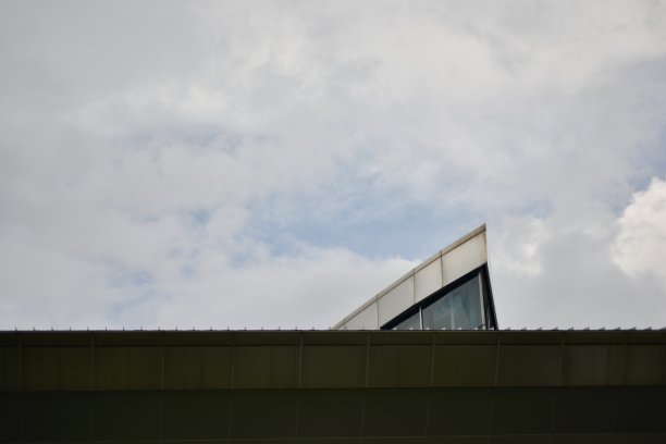 现代建筑上部的照片，三角形的玻璃结构延伸到平坦的屋顶上。图片下载