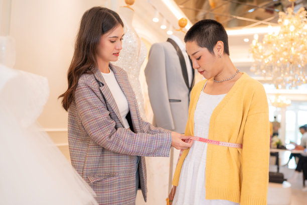 迷人的设计师女孩在婚纱上使用卷尺。图片下载