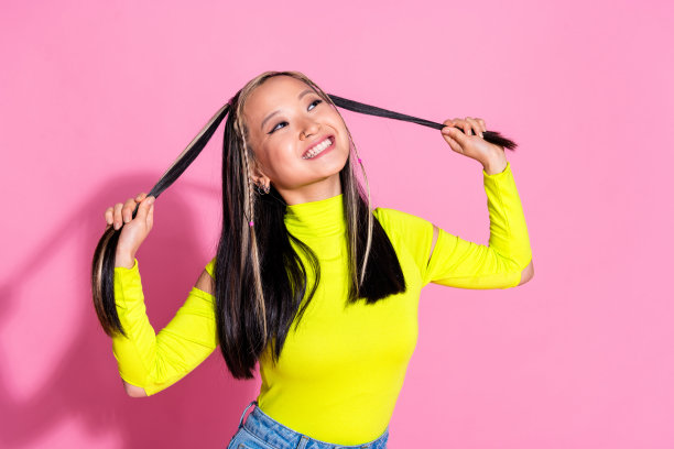 中国女孩染发的照片，穿着黄色高领毛衣，伸出舌头，在粉红色的背景上分开辫子图片下载