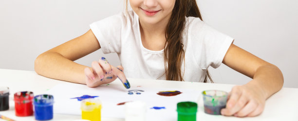 一个小女孩在相册里用毛笔画画，微笑着，一个快乐的孩子在家里的桌子上画水粉画。图片下载