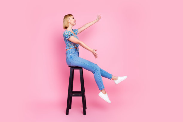 漂亮的年轻女孩的全尺寸照片，坐在凳子上，看空空间，穿上衣孤立在粉红色的背景。图片下载