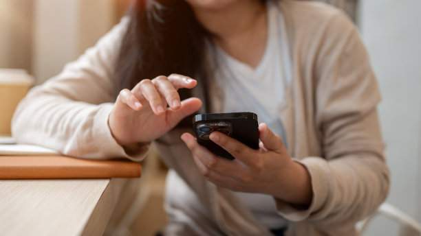 一张裁剪过的照片上，一位亚洲女性坐在一家极简主义咖啡店的桌子旁，正在使用她的智能手机。图片下载