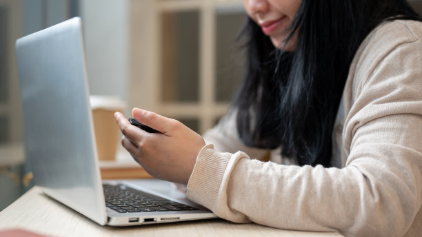 一名亚洲女性在咖啡店远程工作时使用智能手机的特写照片。图片下载