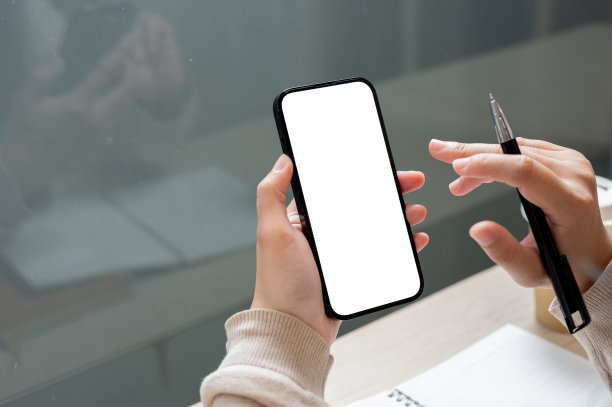 这是一张特写照片，一个女人的手拿着一支笔和一部智能手机，上面有一个白色的屏幕模型。图片下载