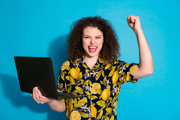 欢快可爱的女孩穿着时髦的热带印花衣服，拿着上网本，在蓝色背景上孤立的照片图片下载