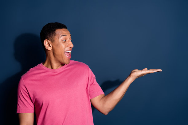 照片的年轻时髦的积极男子在粉红色的t恤广告大惊喜命题孤立在深蓝色的背景图片下载