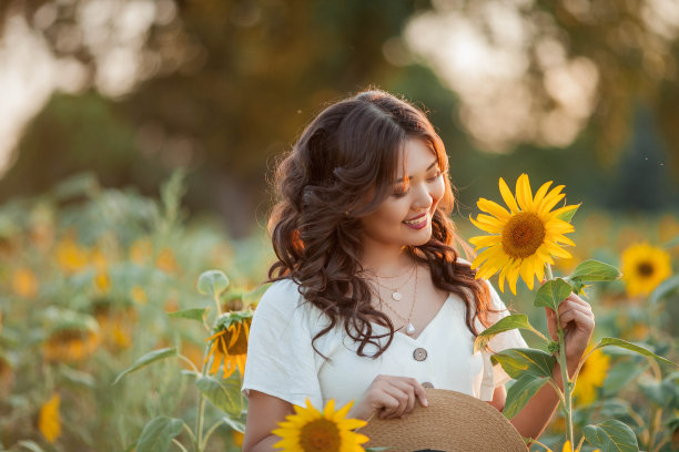 日落时分，年轻的亚洲卷发女子站在向日葵地里。一个年轻美丽的亚洲女人在阳光下的肖像。图片下载