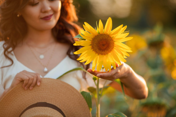 日落时分，年轻的亚洲卷发女子站在向日葵地里。一个年轻美丽的亚洲女人在阳光下的肖像。图片下载