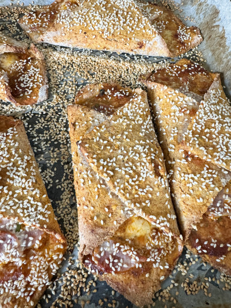 金棕色的全画幅图片，新鲜煮熟的糕点包裹着培根和奶酪，鸡蛋上了釉，上面撒了芝麻，在内衬防油羊皮纸的烤盘上冷却，从高处俯瞰图片下载