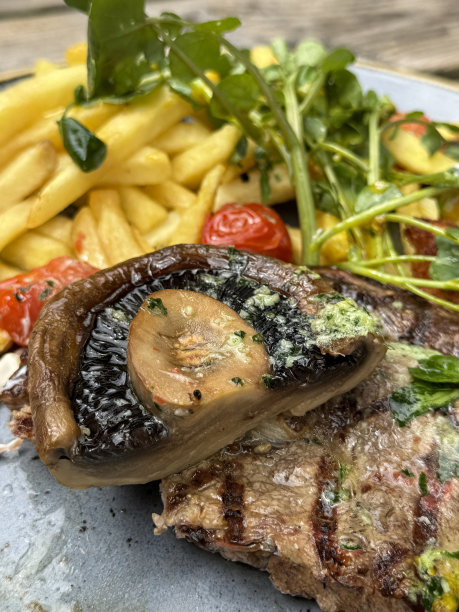 特写图片餐厅餐桌设置与烤黑安格斯西冷牛排与融化的大蒜黄油，炸薯条，圣女果，波多贝罗蘑菇，豆瓣菜，外出就餐，木纹背景，重点在前景图片下载