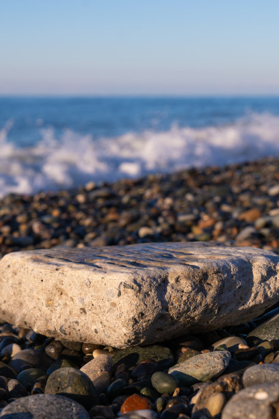 在阳光明媚的日子里，为了在卵石沙滩上插入物体或文字，一块大的扁平石头的特写。垂直图图片下载