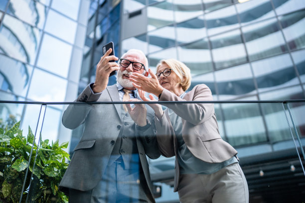 穿着西装的高级男子和成熟的金发女子作为商业伙伴，夫妻朋友或同事聊天，手里拿着智能手机浏览互联网，看照片，交换意见，复制空间图片下载
