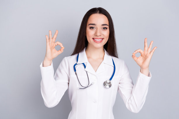 专业医务工作者女士的照片显示大拇指朝上，白色外套孤立在灰色背景上图片下载
