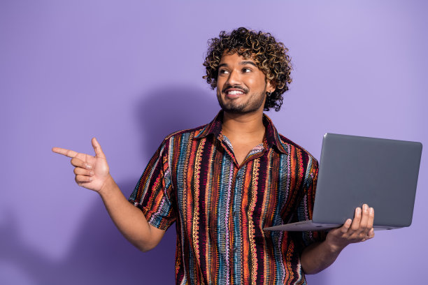 照片中聪明的男人留着波浪发型，穿着印花衬衫，拿着笔记本电脑，在紫色的背景上看着销售空白的空间图片下载