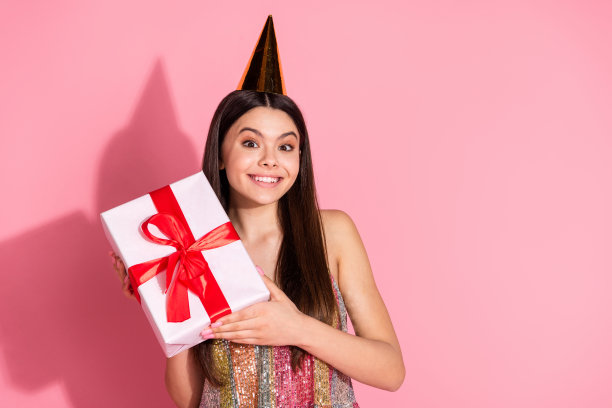 可爱可爱的女孩戴着背心生日帽得到礼物的照片，空白的空间孤立的粉红色背景图片下载