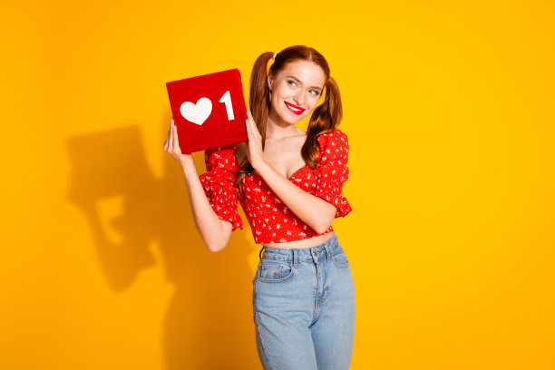 照片肖像迷人的年轻女子看起来感兴趣的心图标穿着时尚的红色衣服孤立在黄色的背景图片下载