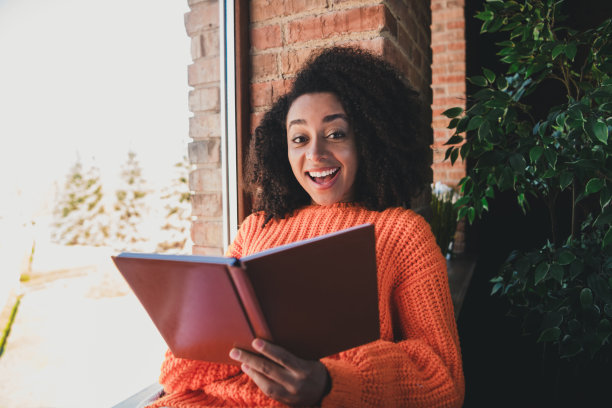 可爱可爱的女士穿着橙色毛衣阅读故事的照片，享受周末在室内房间图片下载