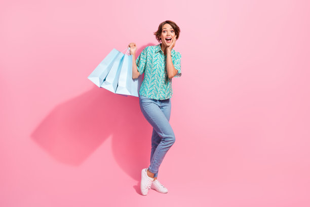 印象深刻的全尺寸照片积极的女孩拿着商店的袋子，手触摸脸颊隔离在粉红色的背景图片下载
