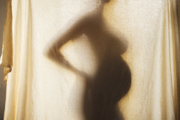 有质感的织物后面，一个孕妇的影子剪影。图片下载