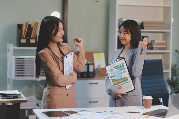 两名年轻女子一起在数码平板电脑上工作的照片。创意女性高管们在办公室里用平板电脑微笑着开会。图片下载