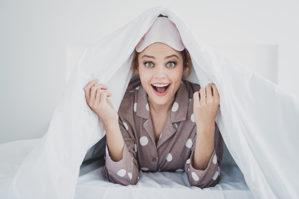 兴奋的好心情的女人的照片，睡衣面具，在温暖的毯子下放松的床在室内的房子公寓房间图片下载