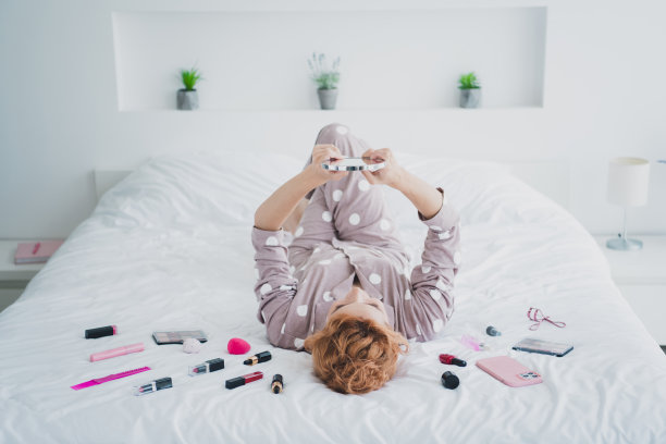 漂亮的年轻女孩的全尺寸照片，躺在舒适的床上，照镜子，穿睡衣，卧室在室内图片下载
