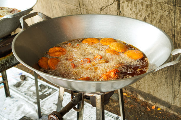 泰国清迈一家街头小吃店，用大平底锅高温煎腌猪肉和鸡肉的图片。图片下载