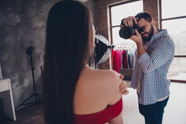 照片微笑的摄影师拍摄肖像的可爱的女士穿着红色礼服在室内工作室的工作场所图片下载
