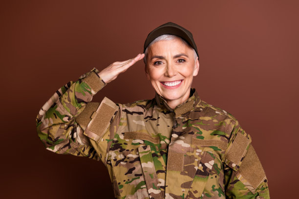照片迷人的微笑老太太穿着迷彩制服显示你的荣誉手势空的空间孤立的棕色背景图片下载