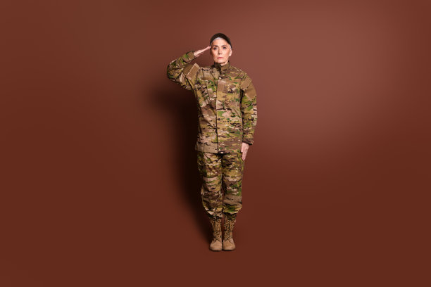 漂亮的资深女性勇敢的女军人敬礼穿着迷彩军服孤立的棕色背景的全尺寸照片图片下载