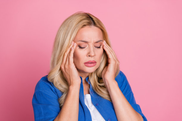 照片中压力大、心情低落的女人穿着蓝色衬衫，双臂太阳穴空着，与世隔绝的粉红色背景图片下载