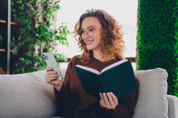 迷人可爱的成功女人的照片，穿着时尚的衣服，拿着书，从家里舒适的客厅，在室内的房子图片下载