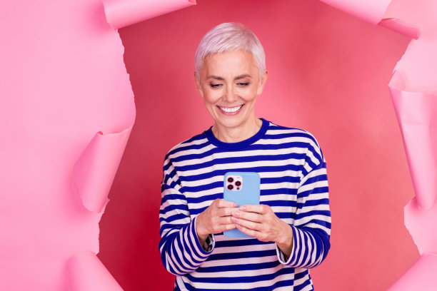 照片迷人开朗可爱的资深女博主穿着时尚的衣服打破纸墙孤立在粉红色的背景图片下载