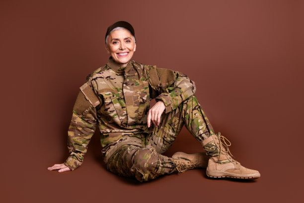 资深女勇敢的女军人的全尺寸照片，轻松地坐在地板上，穿着迷彩服，孤立在棕色背景上图片下载