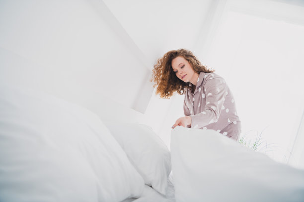 漂亮的年轻女孩穿着睡衣铺床的照片明亮的室内卧室公寓室内图片下载