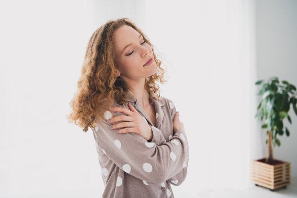 照片中漂亮的年轻女孩闭着眼睛抱着肩膀穿着睡衣明亮的室内卧室公寓室内图片下载