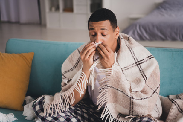 照片不健康的心烦意乱的家伙睡衣睡衣微笑呆在家里沙发擤鼻涕在室内房子公寓房间图片下载