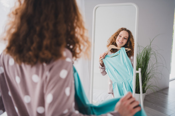 漂亮的年轻女孩的照片拿着裙子照镜子穿睡衣明亮的室内卧室公寓室内图片下载
