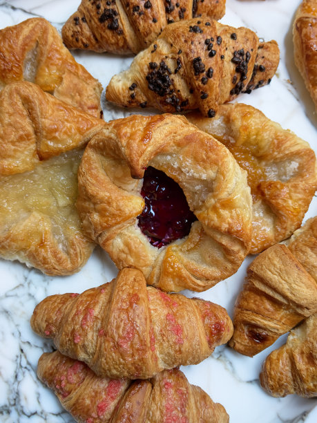 大理石柜台上各种新鲜出炉的早餐糕点的特写图片，覆盆子和杏果酱馅的糕点，巧克力榛子，素食覆盆子和全黄油牛角包，高架视图图片下载
