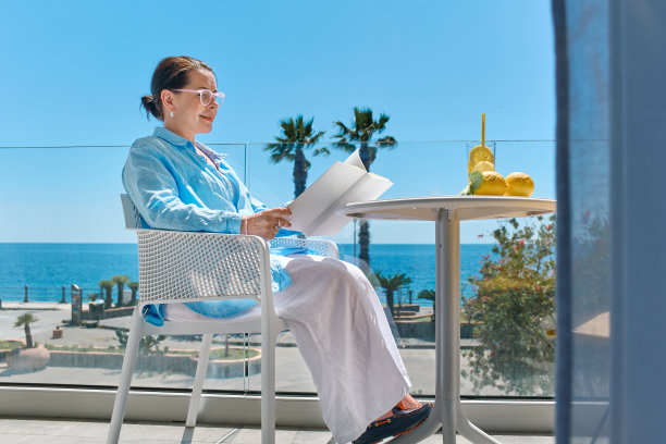 满足的成熟的女人在夏天在酒店阳台上看书，凝视着大海。在地中海放松和暑假的概念。图片下载