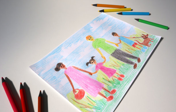 一个孩子用彩色铅笔画画的角度照片。这幅画展示了一个家庭。铅笔周围，白色背景。图片下载